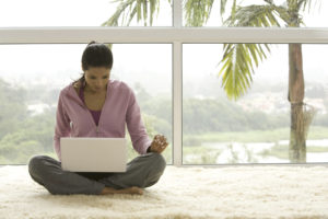 Young woman sitting on rug and using laptop